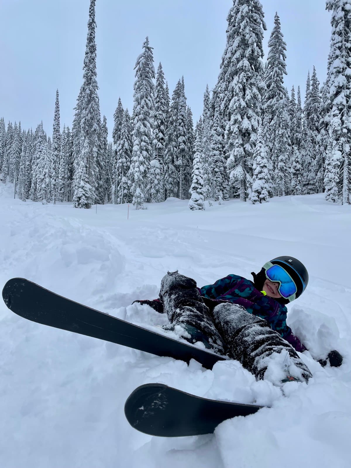 Kid fallen in deep powder snow while skiing, laughing it off and getting back up