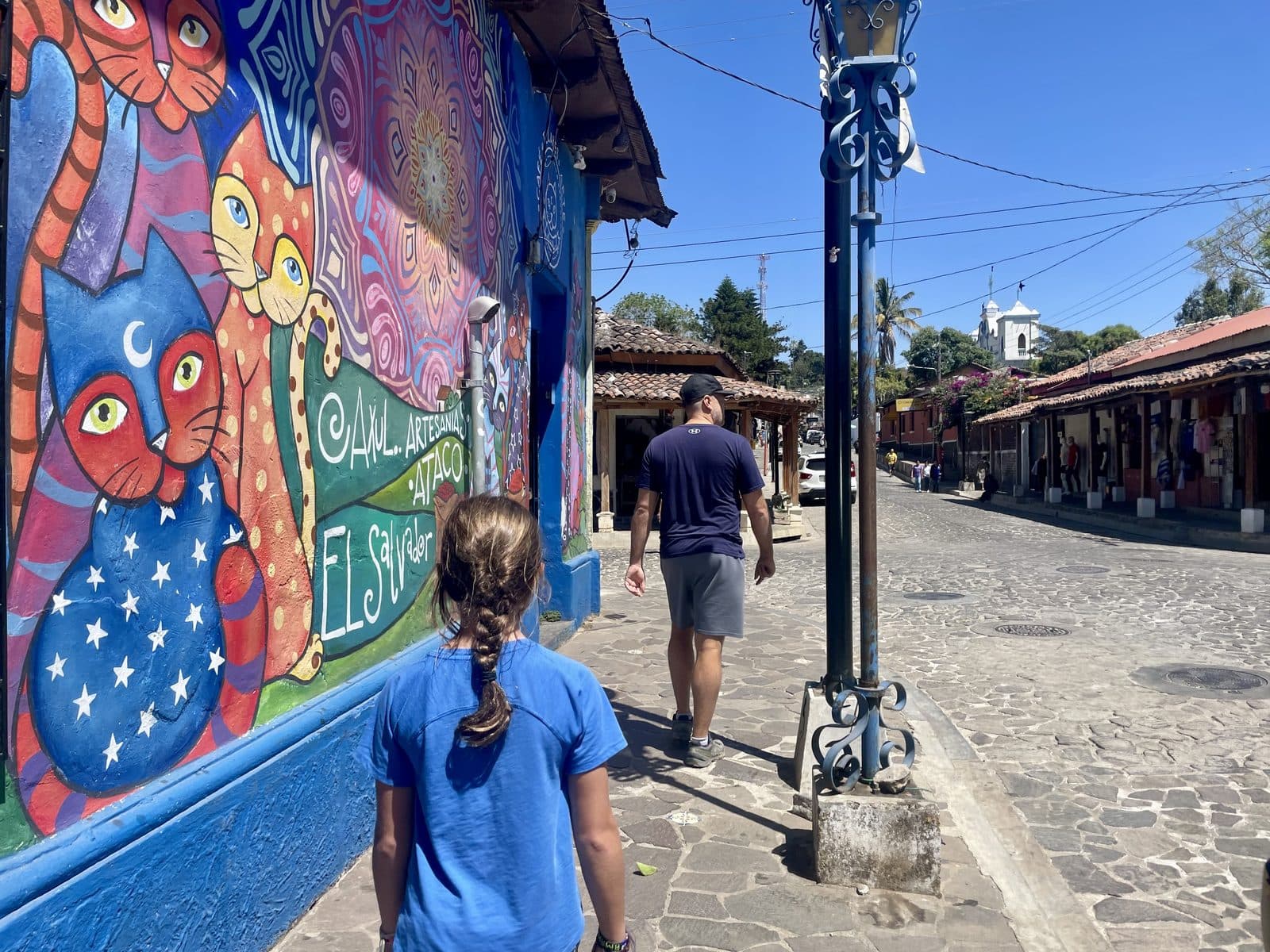 Julia stopping to admire a colourful cat mural on a cobblestone street in El Salvador, curiosity-led learning in action
