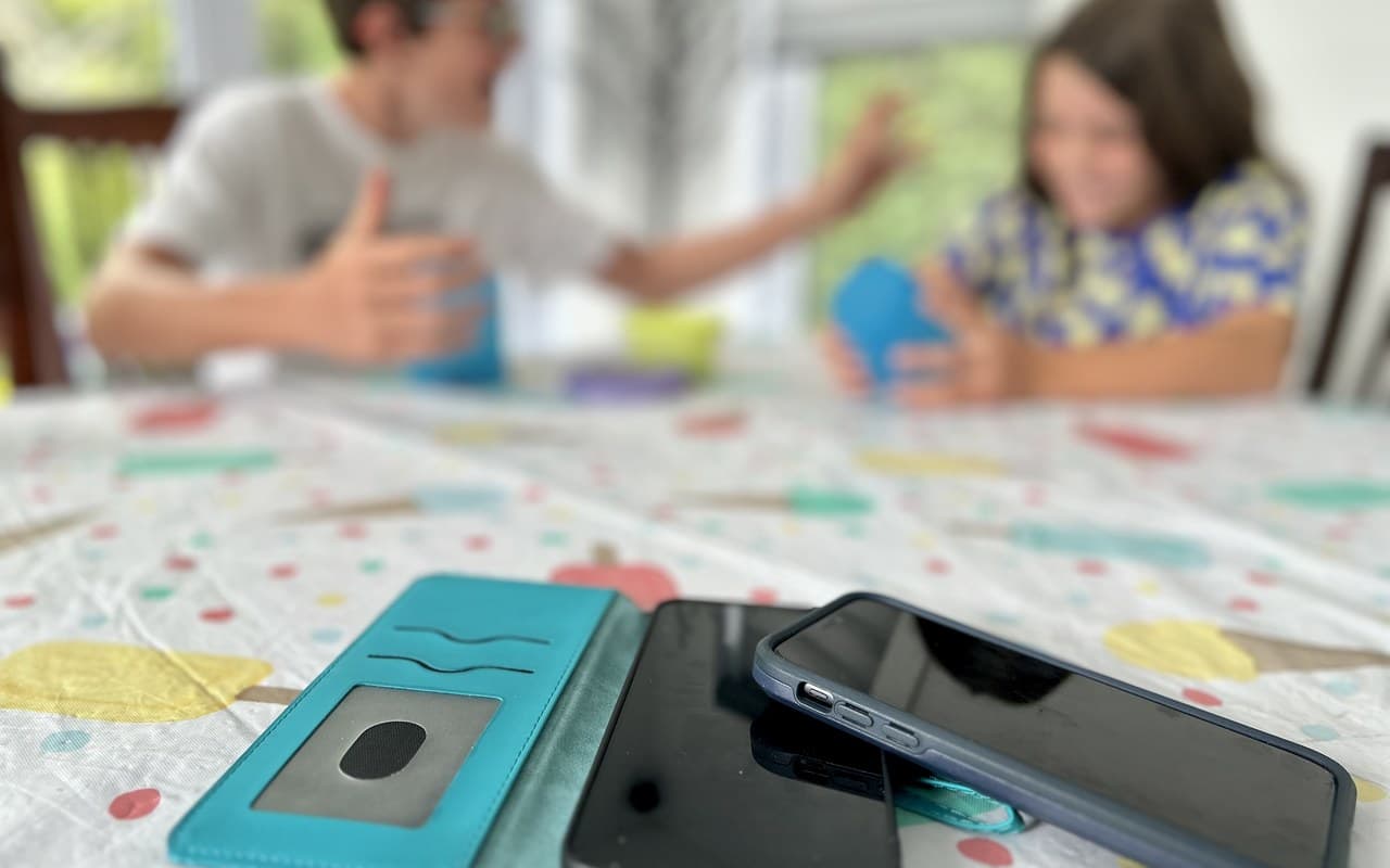 Two phones set face-down on the table in the foreground while two kids play a game together, blurred, behind them, screens set aside for real connection