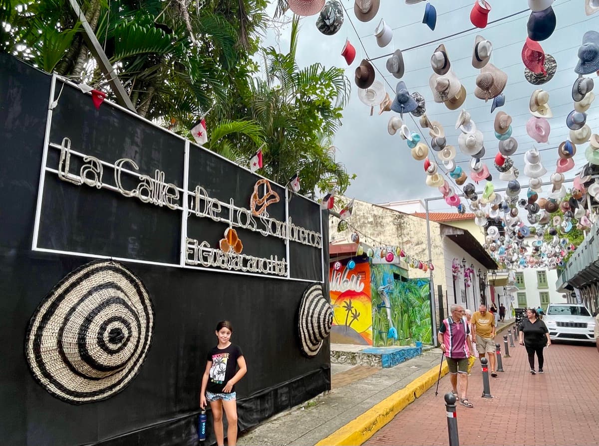 My daughter exploring a colourful street with hanging hats and murals in Panama
