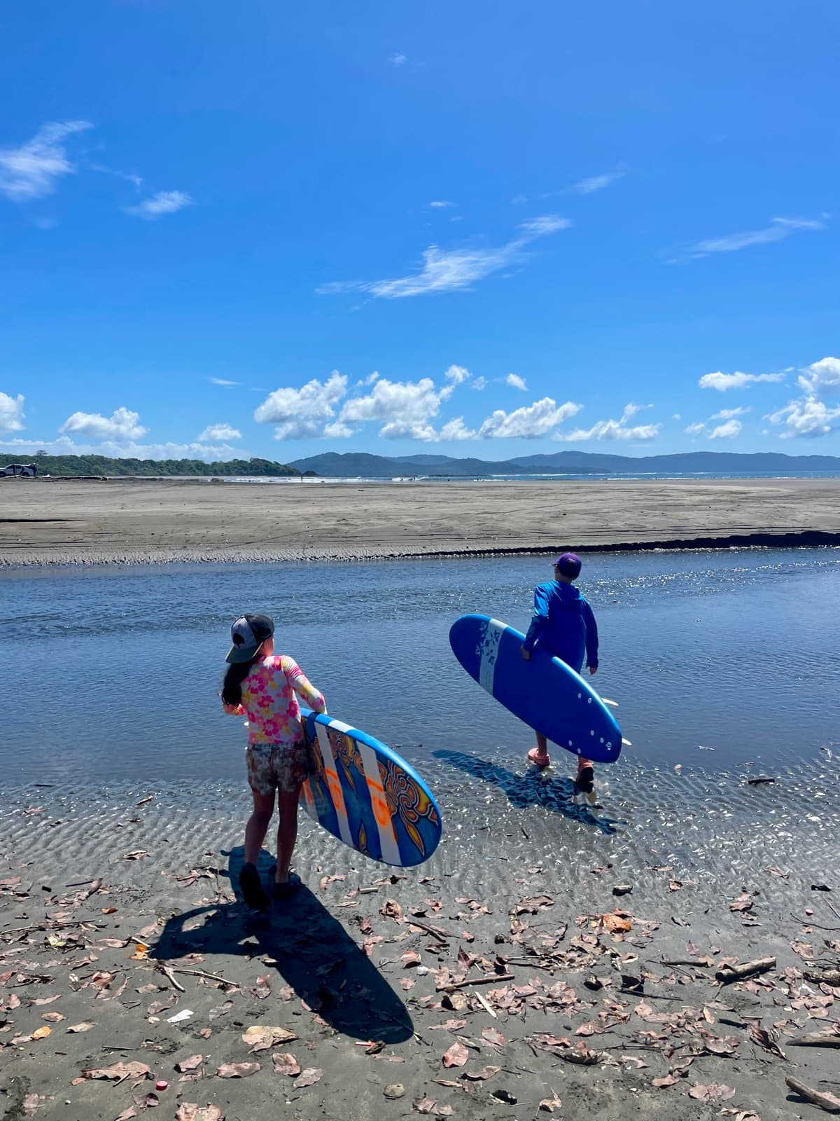 Zach and Julia carrying surfboards across the beach on a sunny afternoon