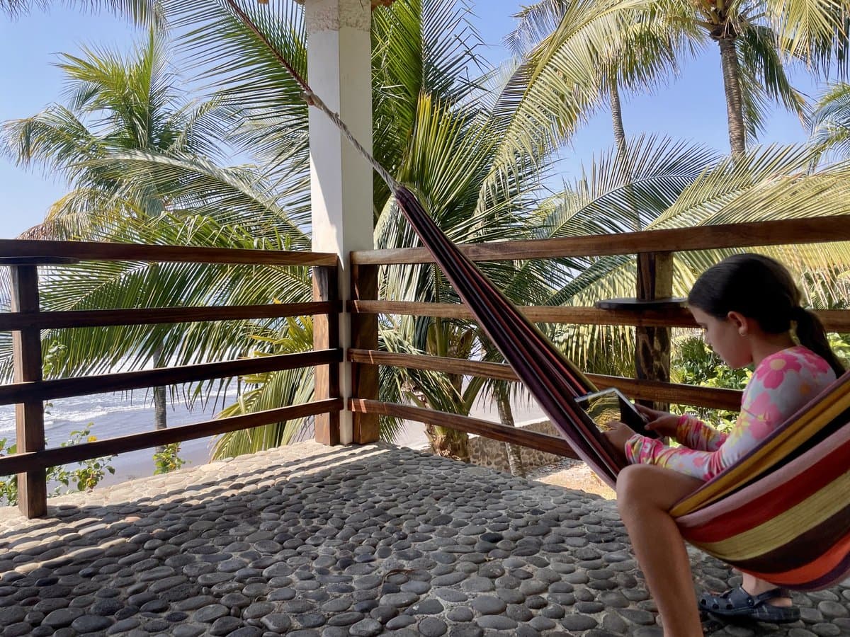 Julia reading in a hammock on a tropical patio with ocean and palm trees behind her