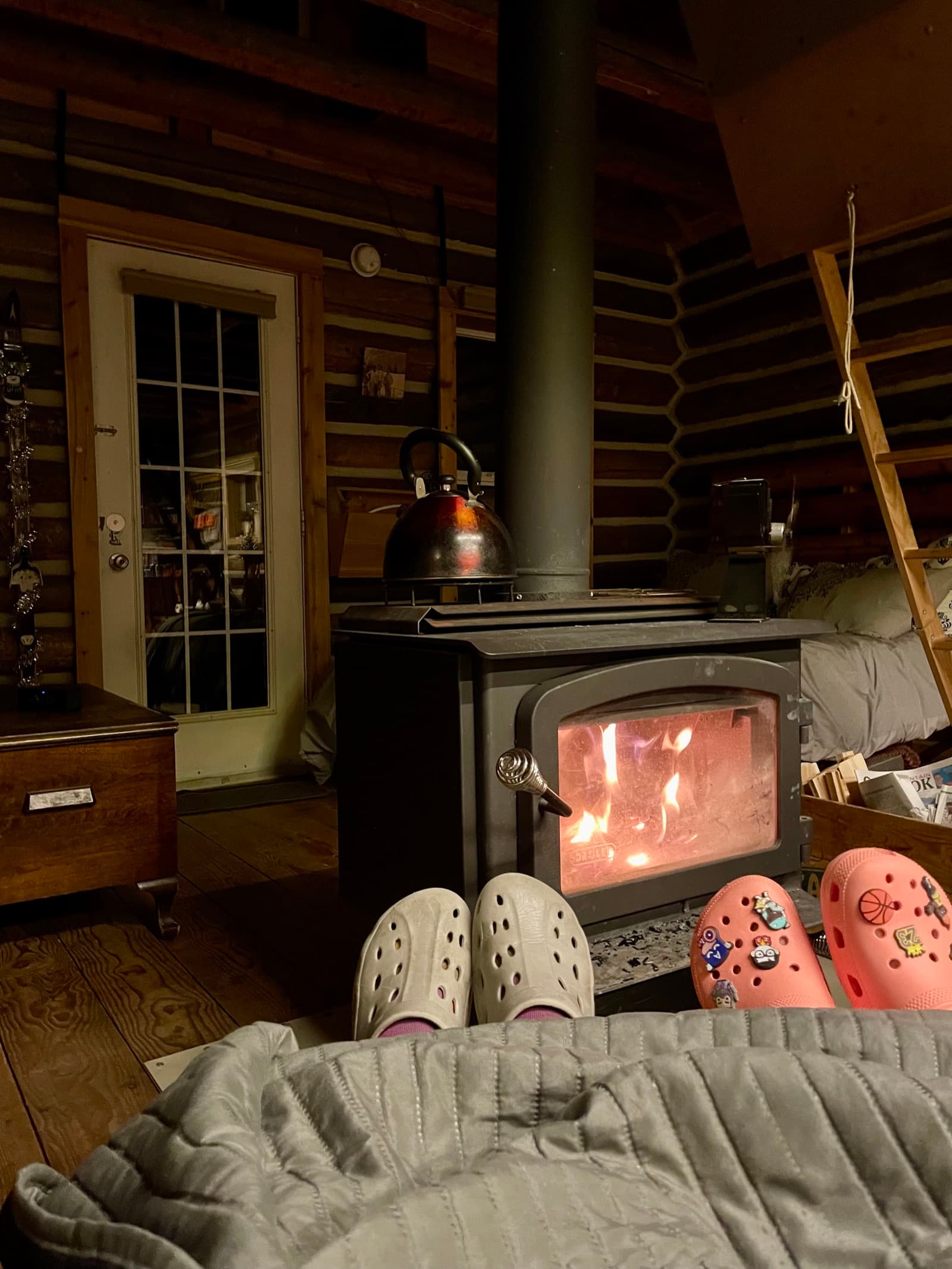 Feet up in front of a wood stove in a cozy cabin, kettle on top, finally resting