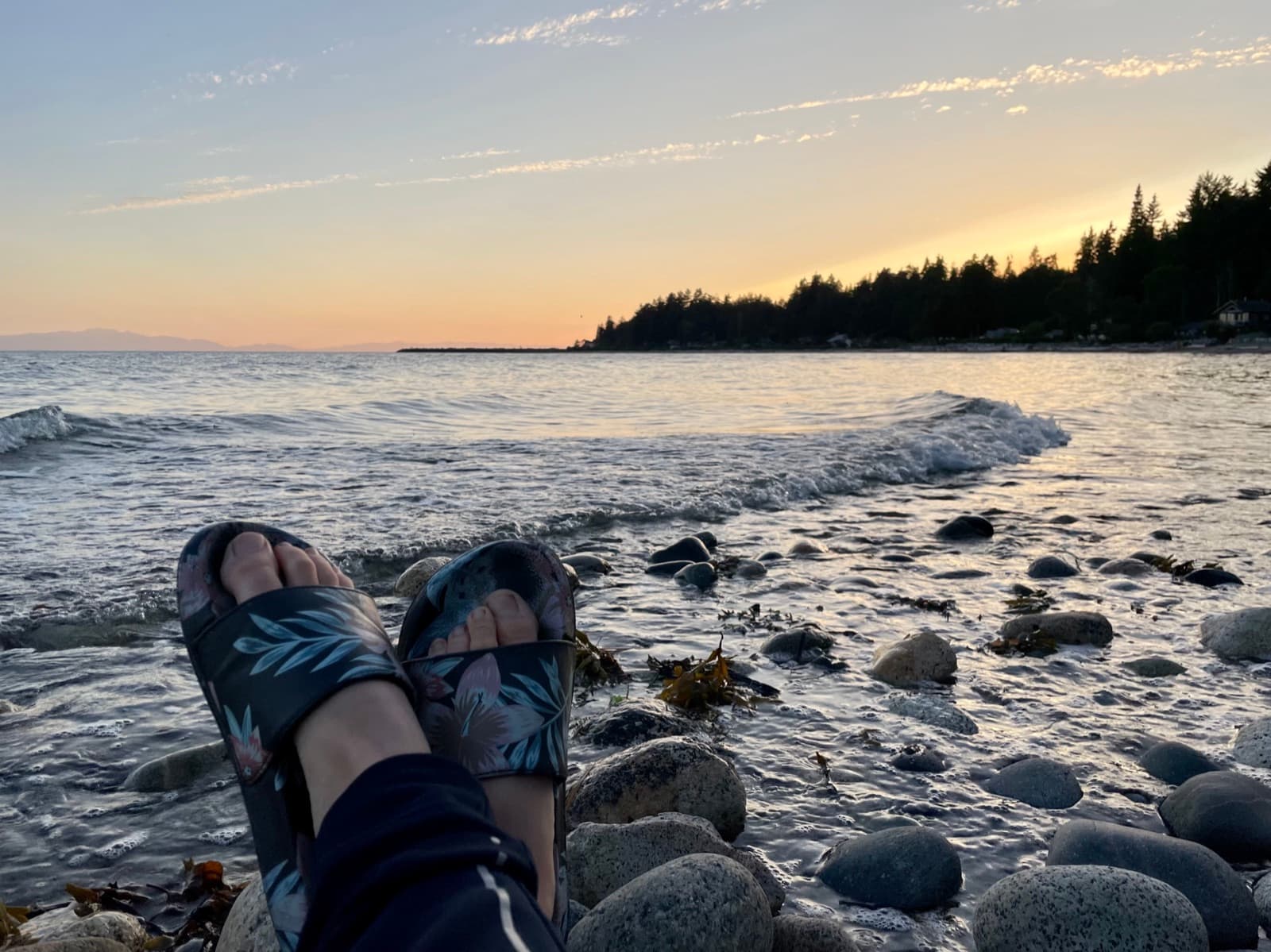 Feet up on the rocks at the edge of the ocean at sunset, the picture of a mom finally taking five minutes for herself